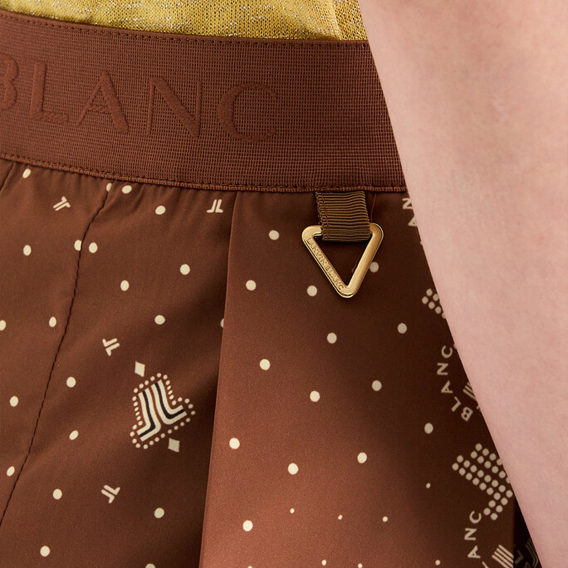 Brown skirt with white polka dots and a brand logo on a person wearing a yellow top.