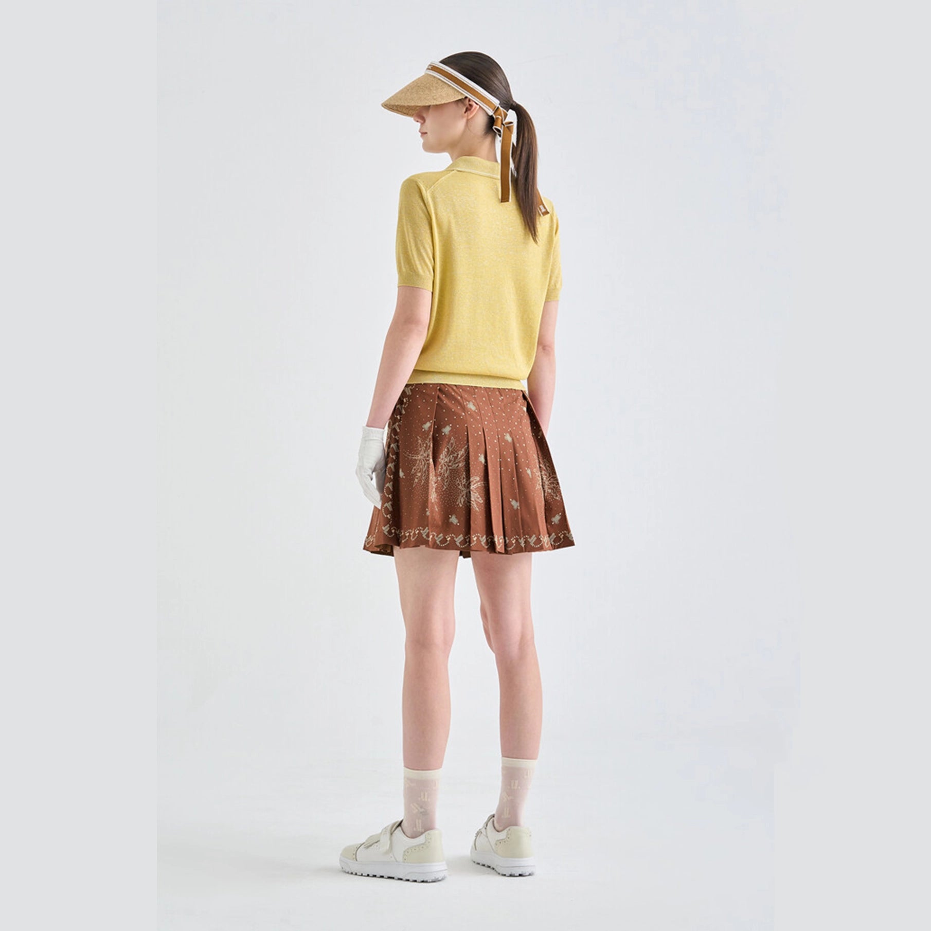 Person wearing a yellow top and brown patterned skirt on a white background