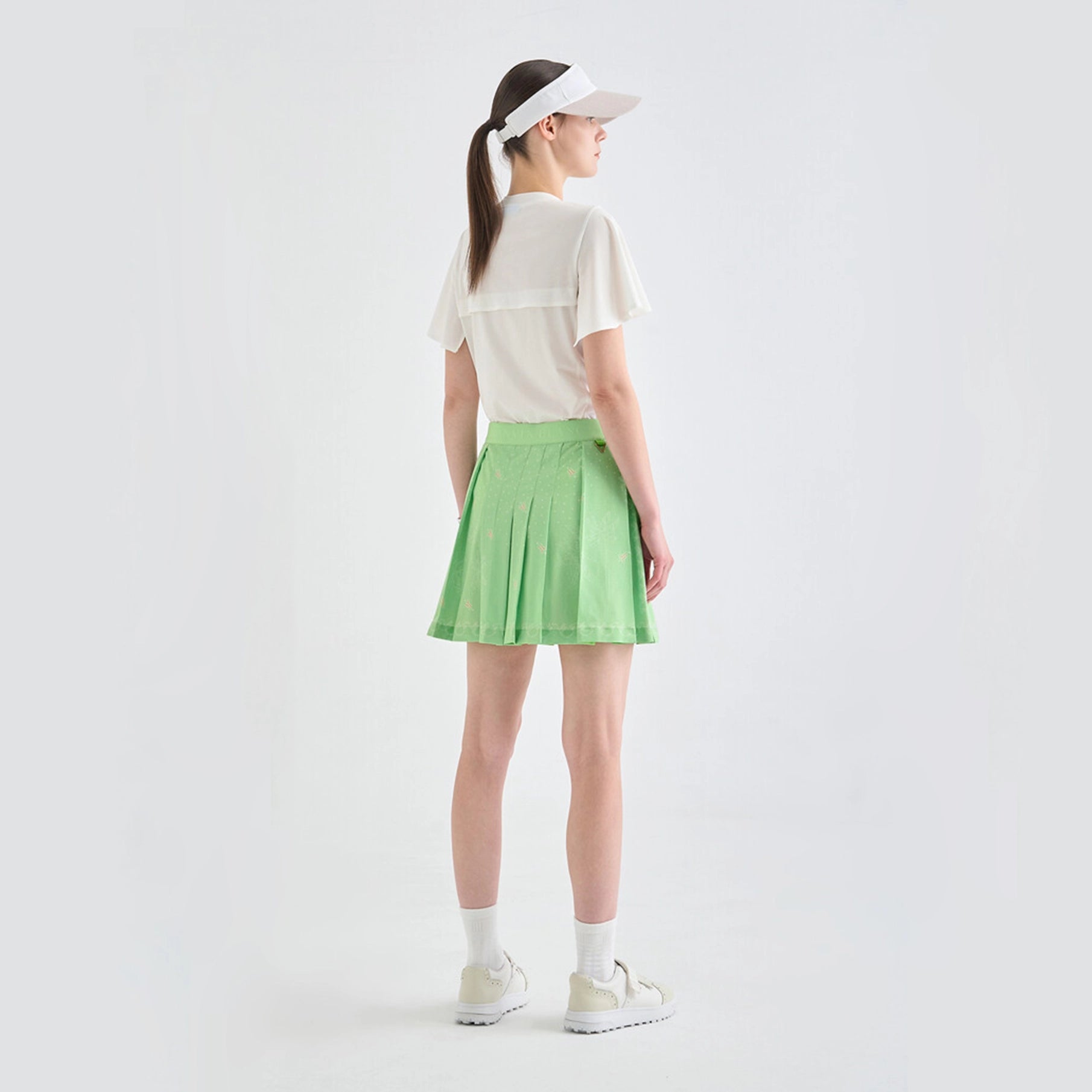 Person wearing a white shirt, green skirt, and visor on a light gray background