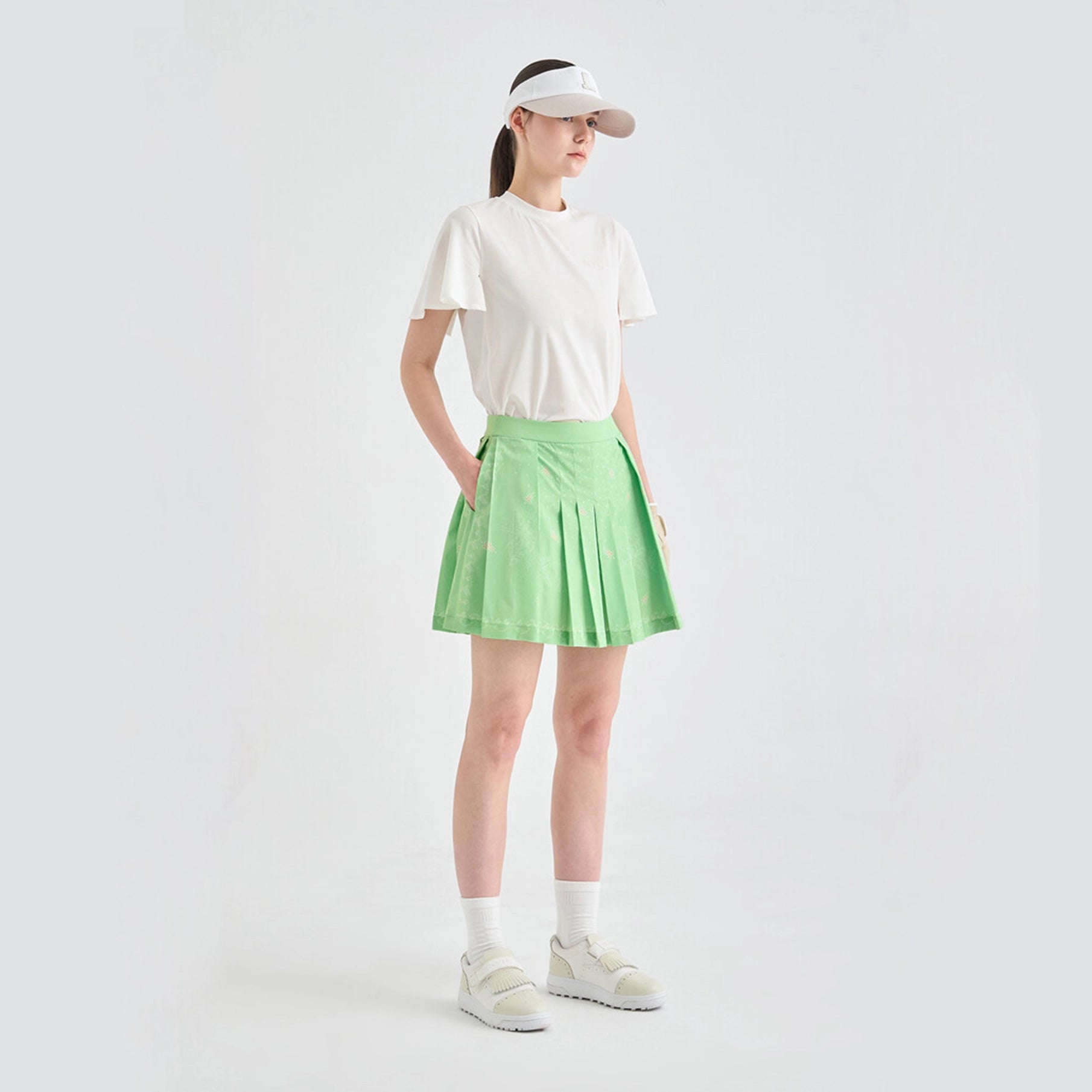 Person wearing a white t-shirt, green pleated skirt, and white sneakers on a light gray background