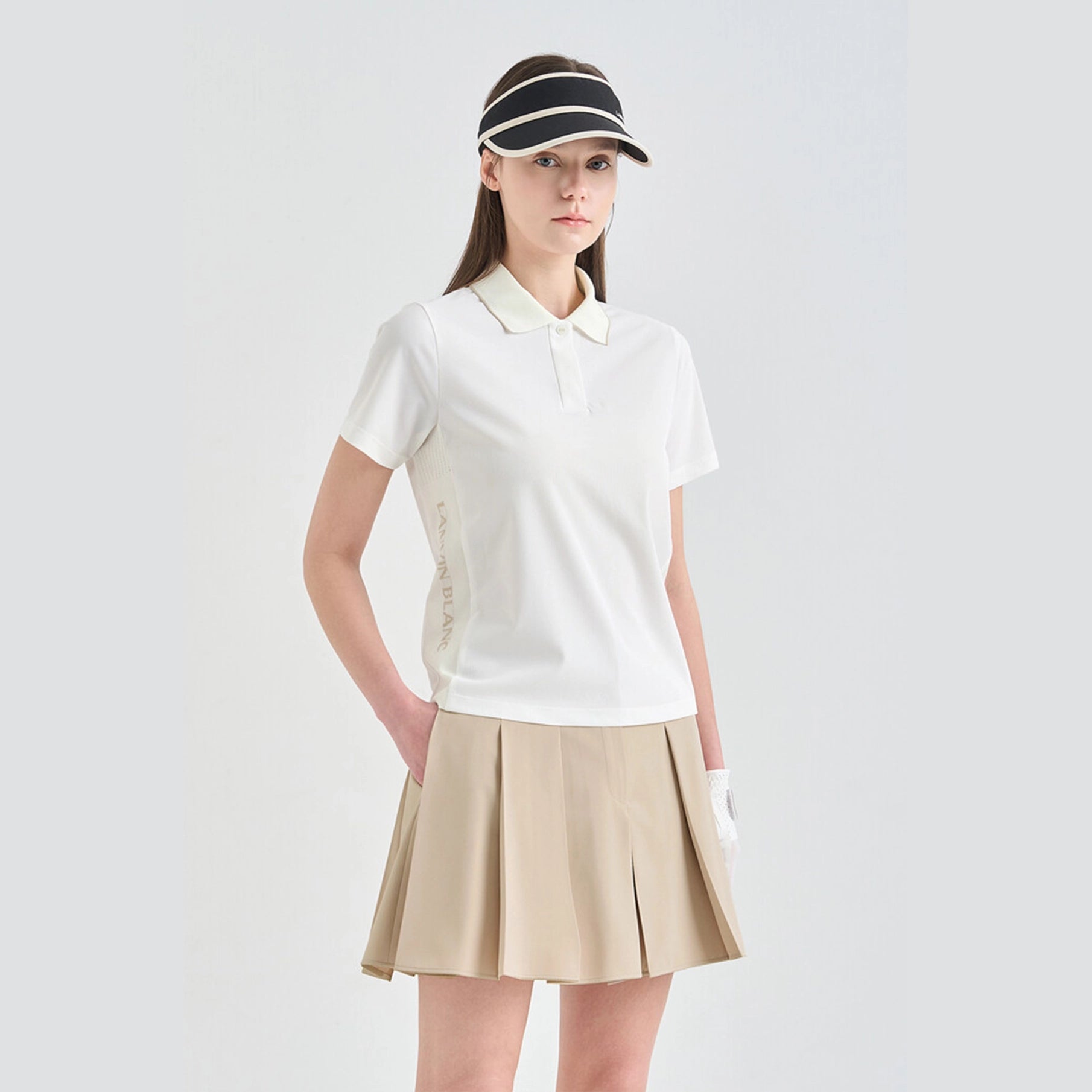 Woman wearing a white polo shirt and beige skirt with a visor on a light gray background