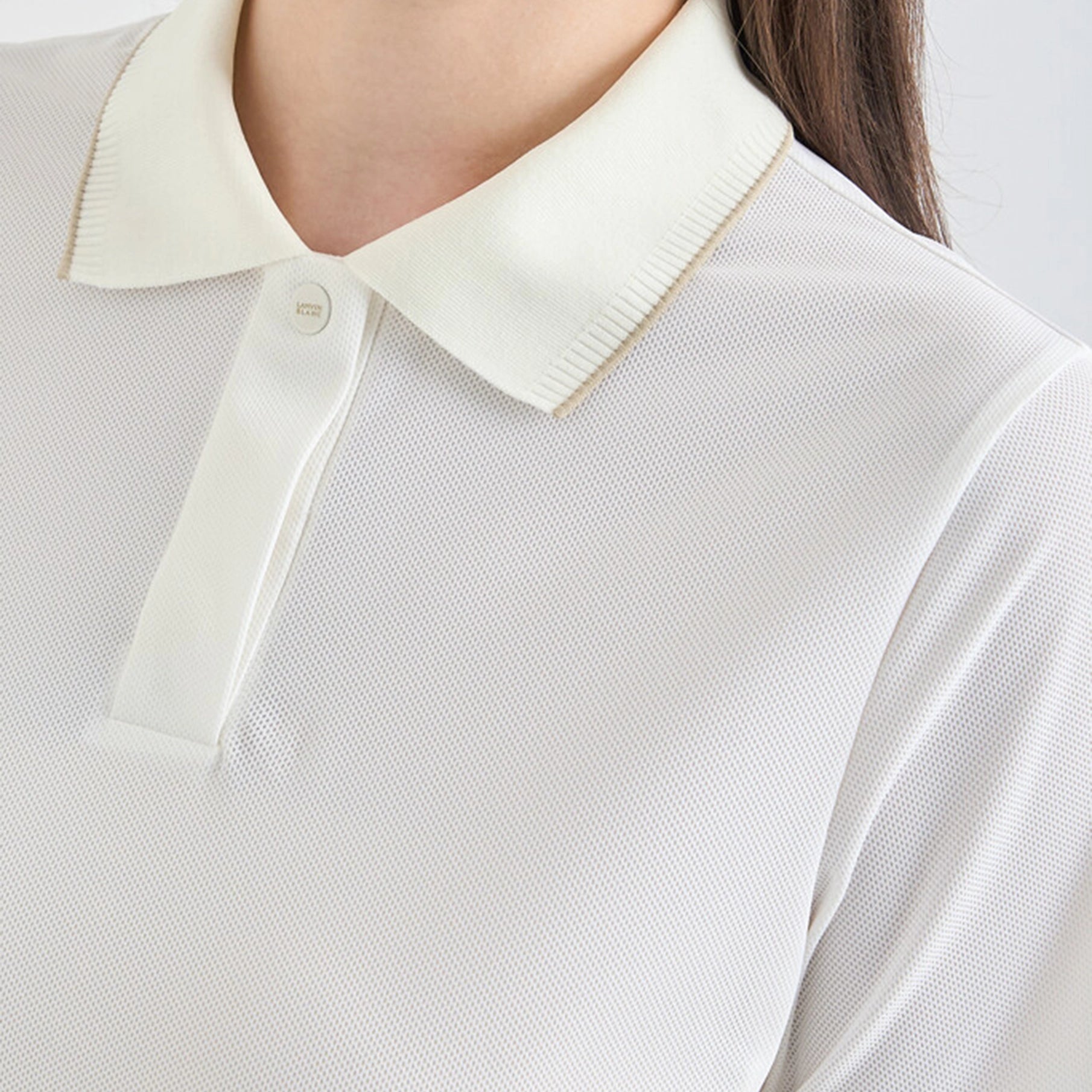 Close-up of a white polo shirt with a cream collar on a plain background