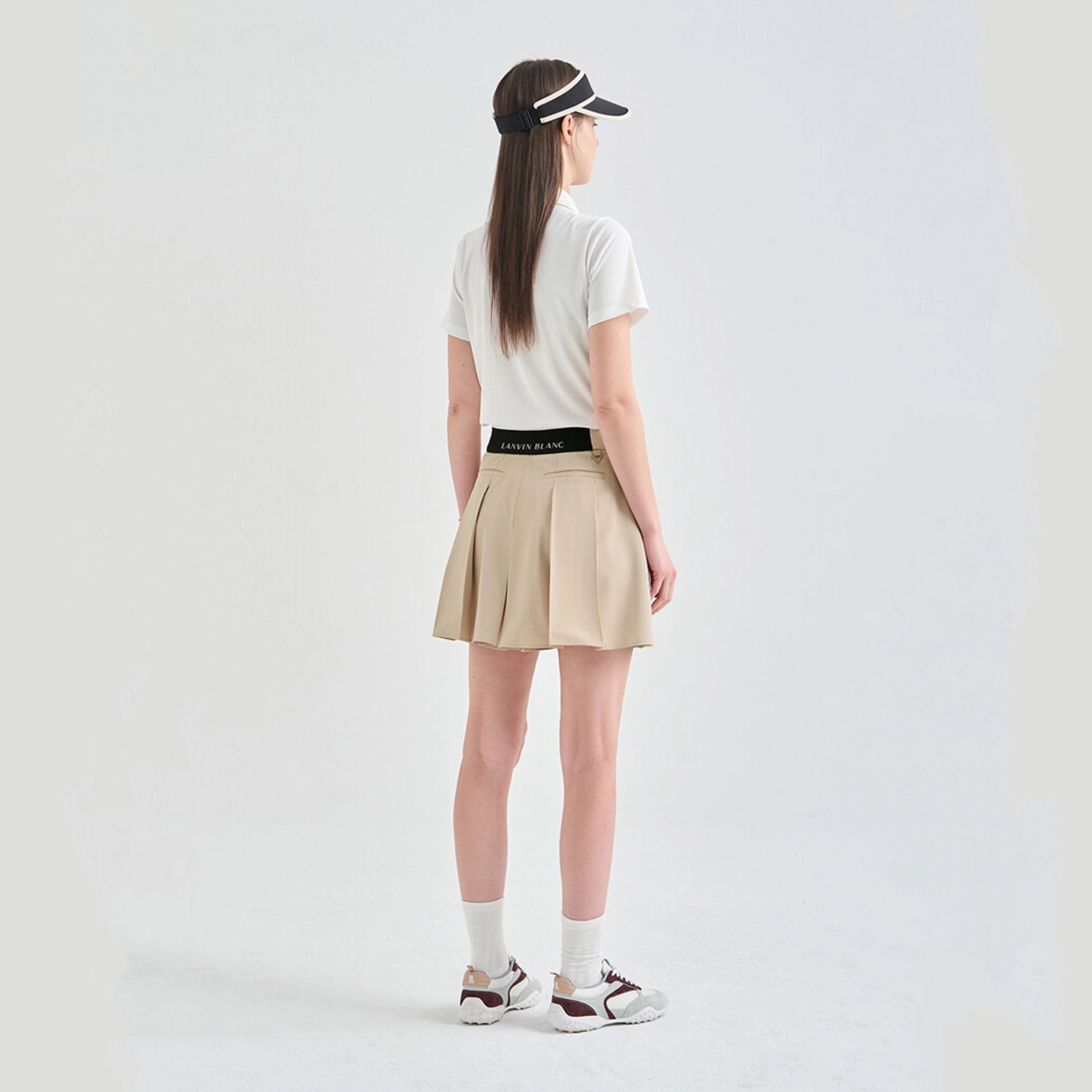 Person wearing a white t-shirt, beige skirt, and visor on a light gray background