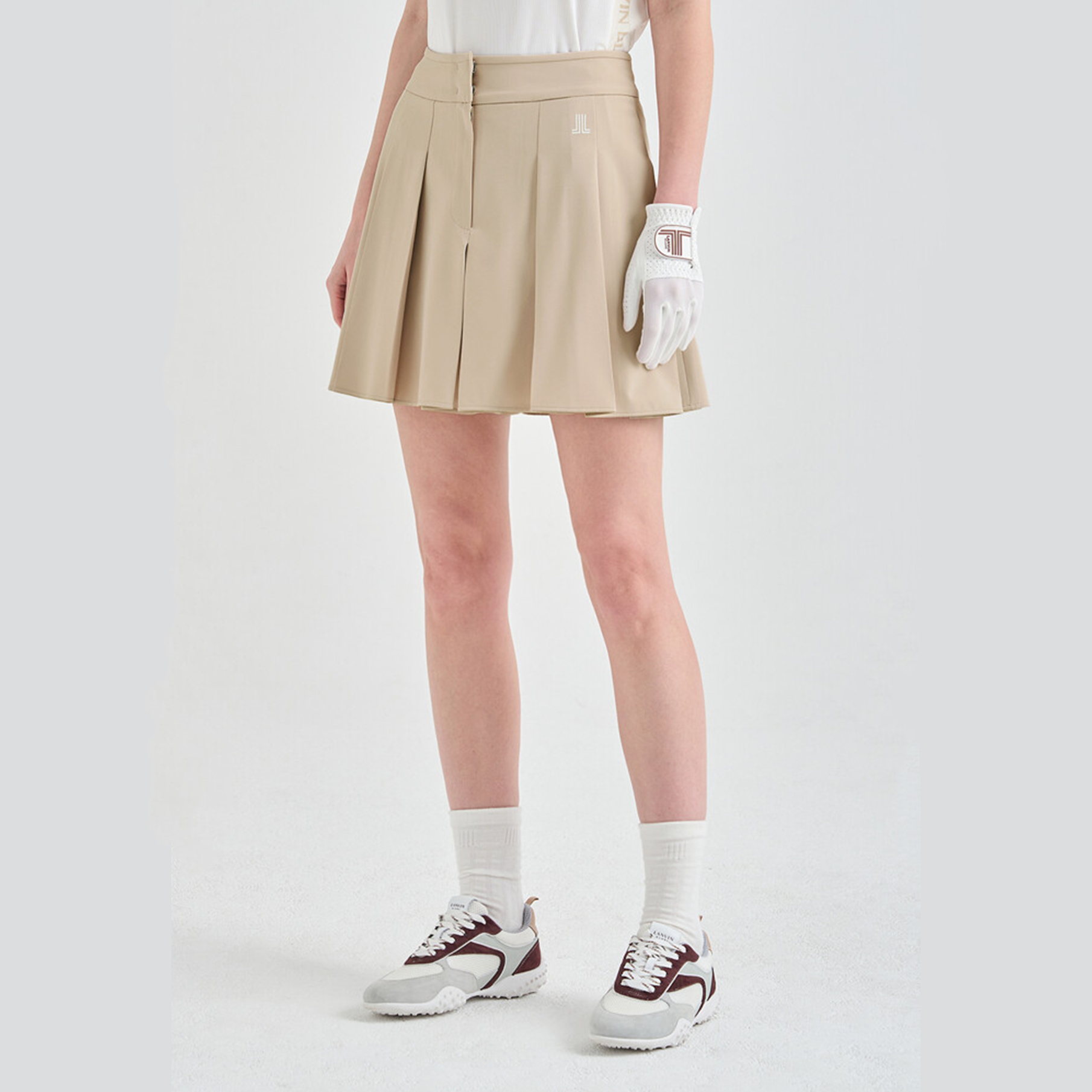 Person wearing a beige pleated skirt, white shirt, white gloves, and maroon and white sneakers on a light gray background
