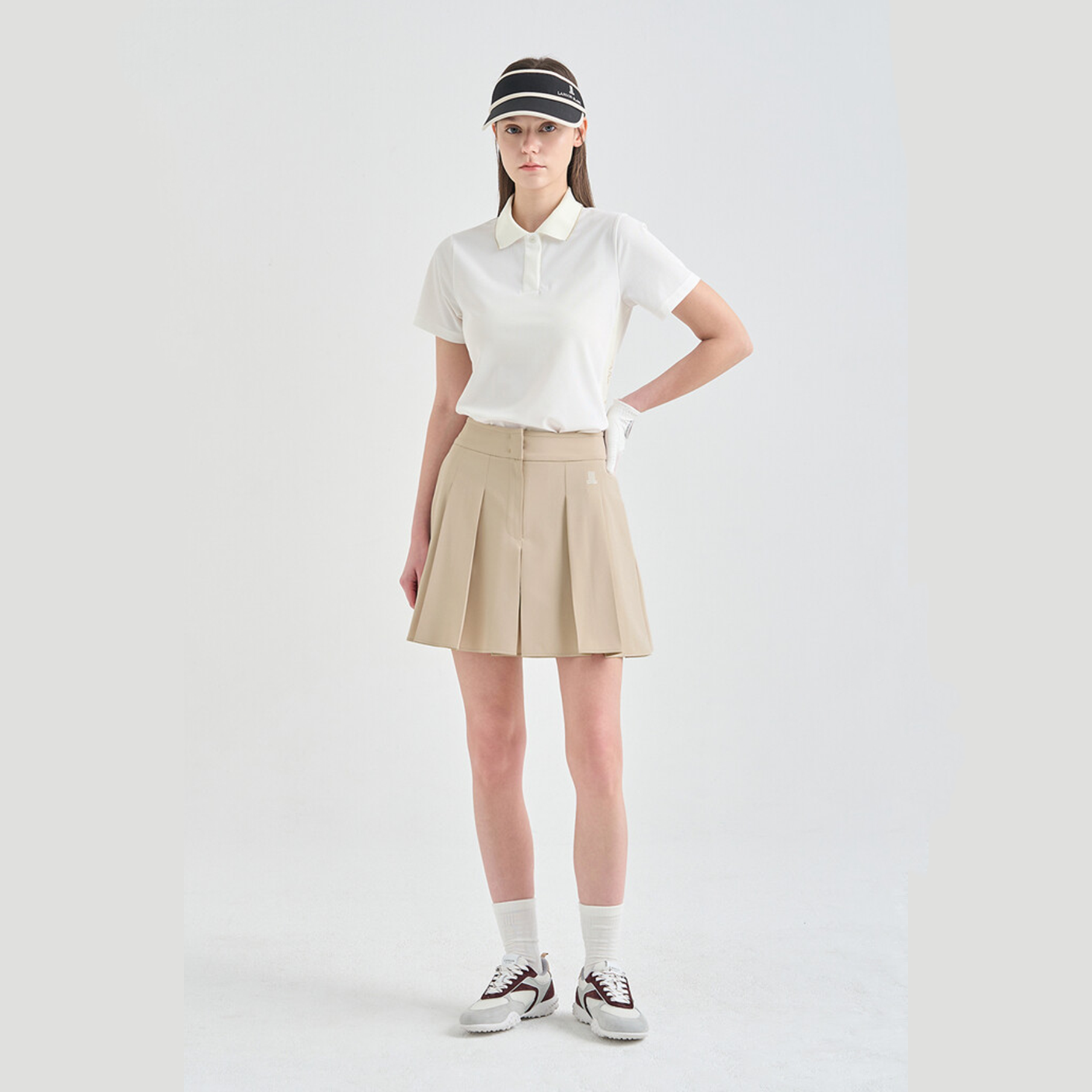 Person wearing a white polo shirt, beige skirt, and black shoes on a white background