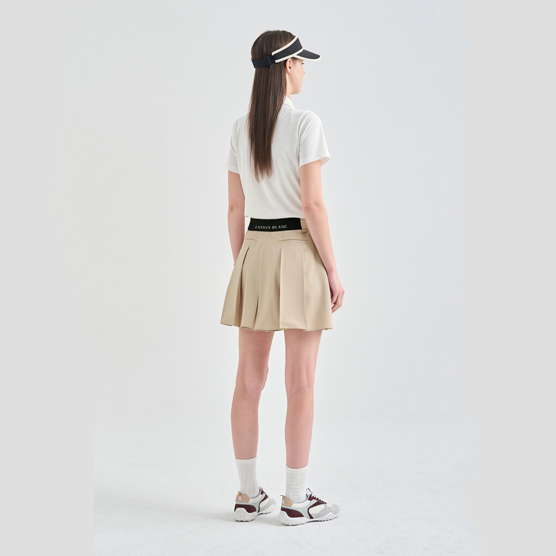 Person wearing a white t-shirt, beige pleated skirt, and visor on a plain background