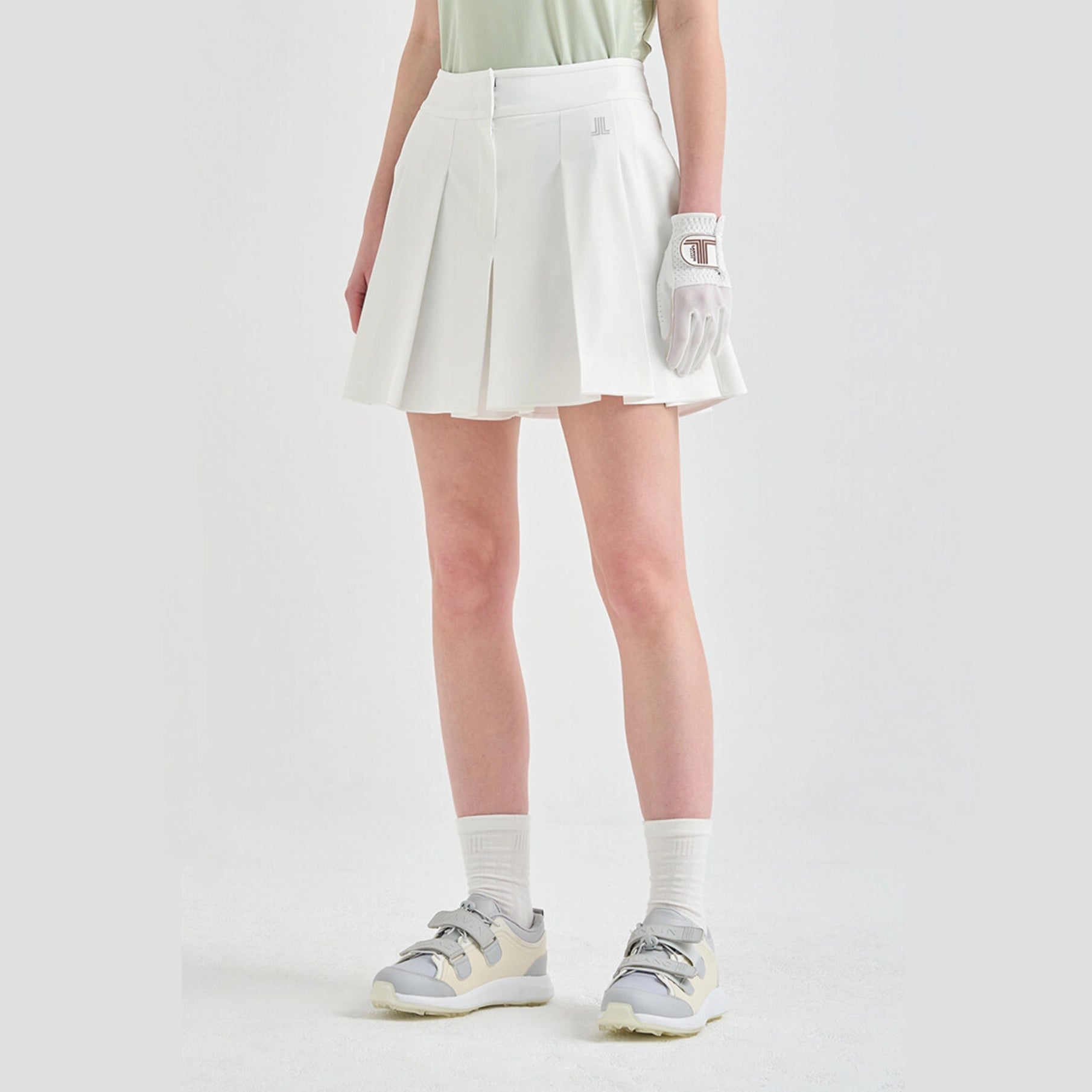 Person wearing a white pleated skirt, white golf glove, and gray shoes on a light gray background