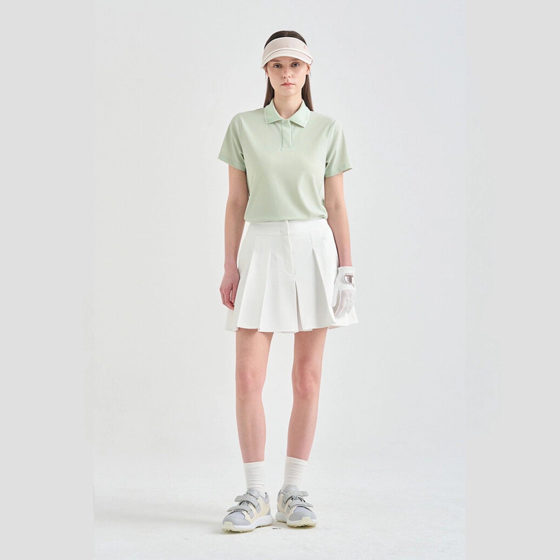 Person wearing a light green polo shirt, white skirt, visor, and gloves on a white background