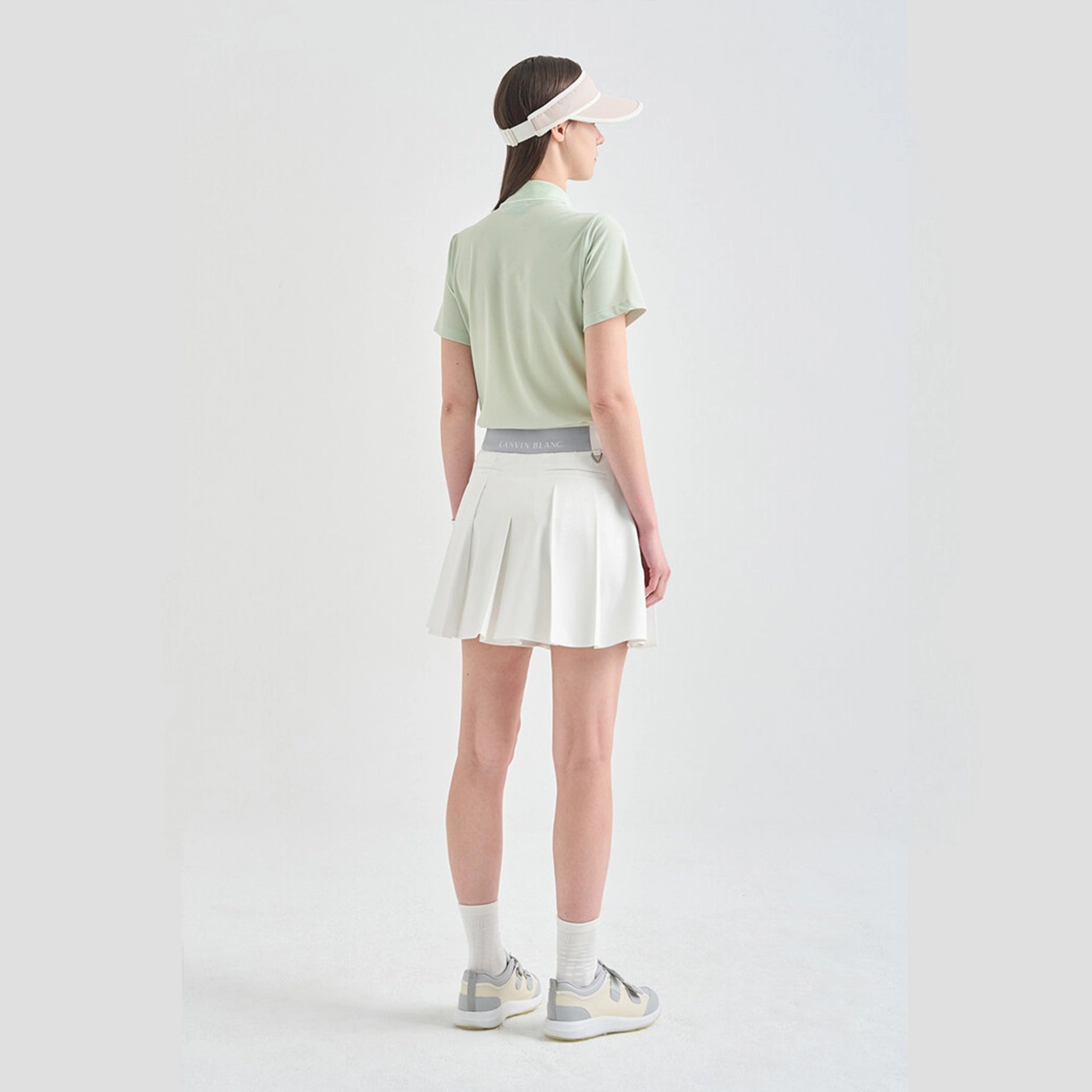 Person wearing a light green polo shirt, white skirt, and visor on a plain background
