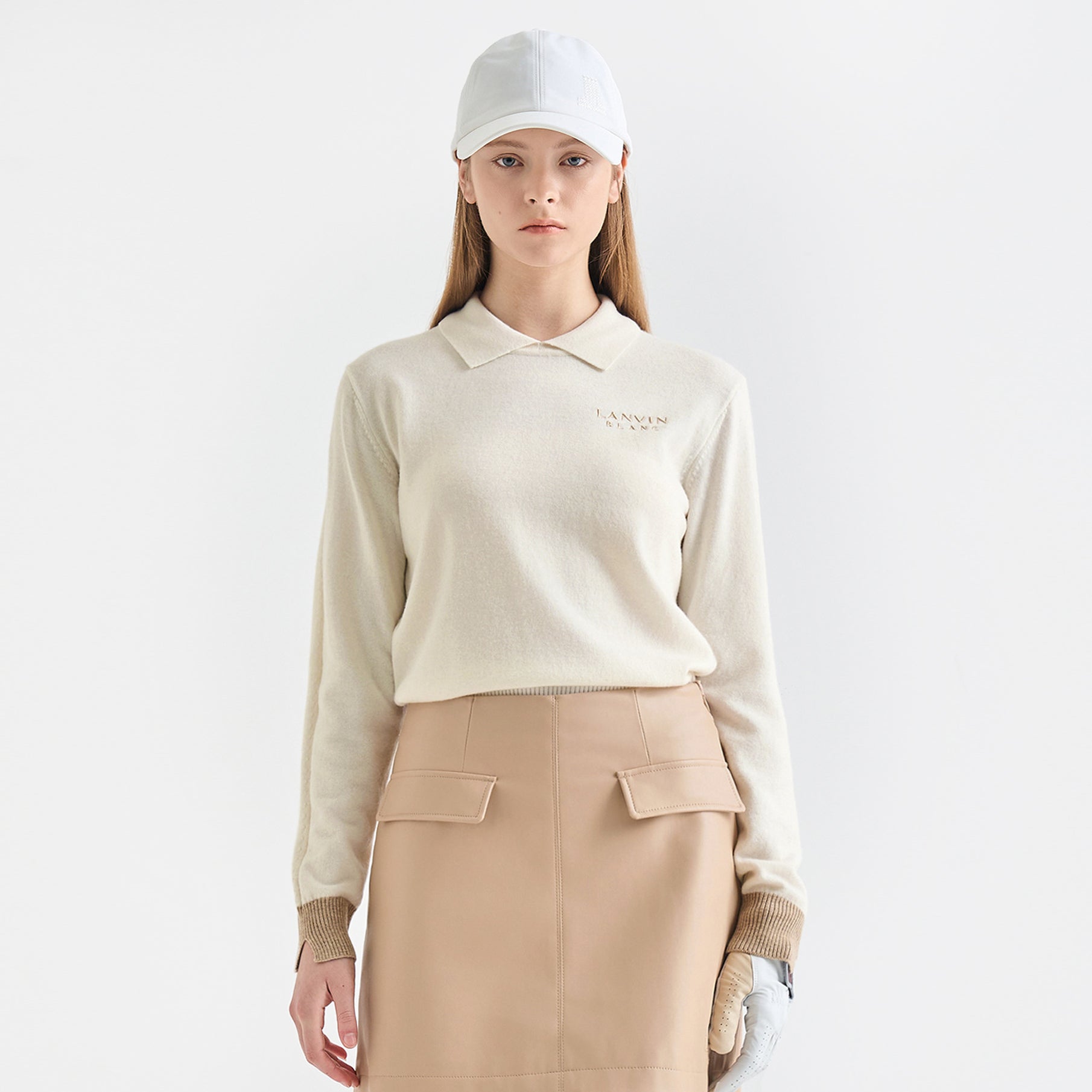 Person wearing a cream sweater and beige skirt with a white cap on a light gray background