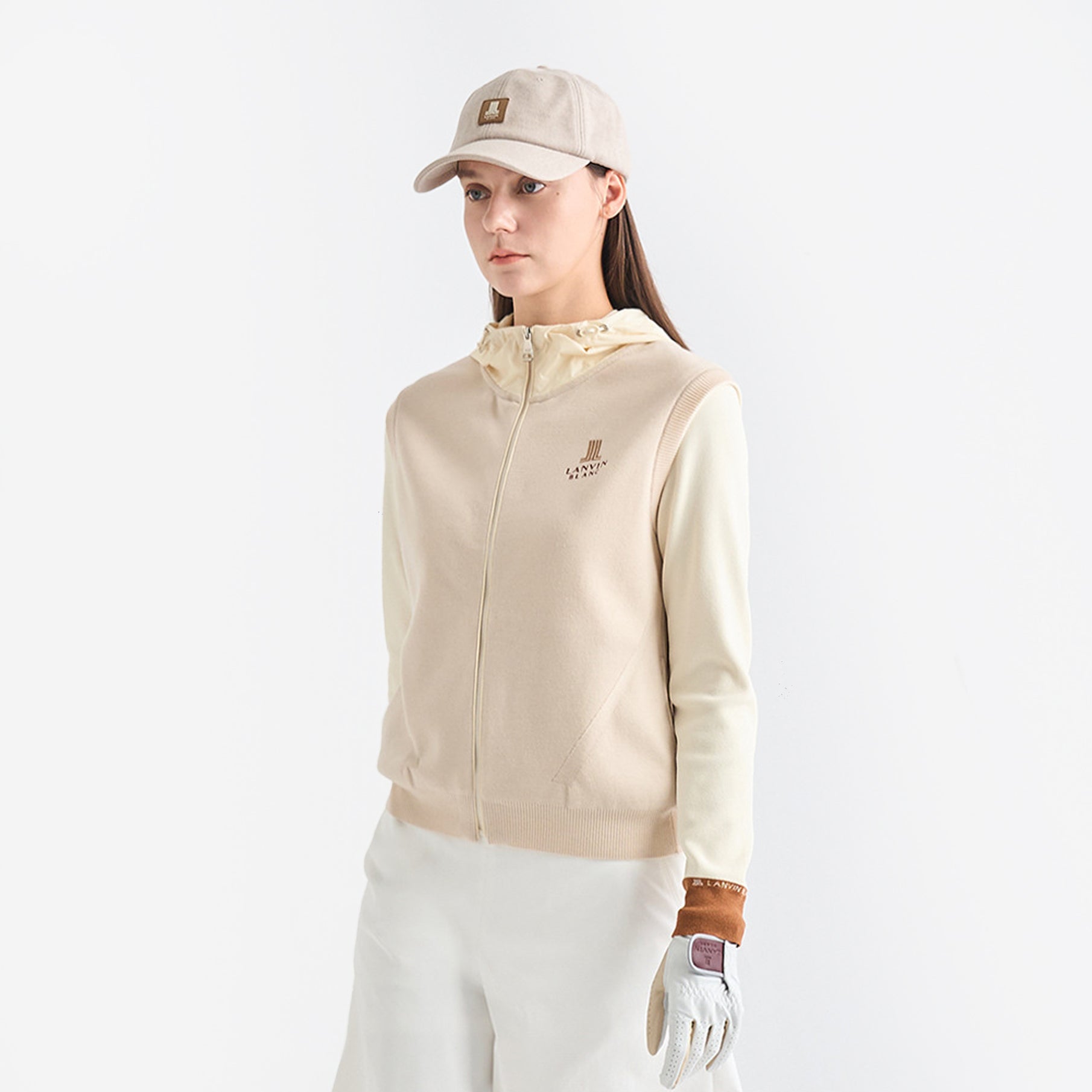 Woman wearing a beige golf jacket, cap, and gloves on a white background