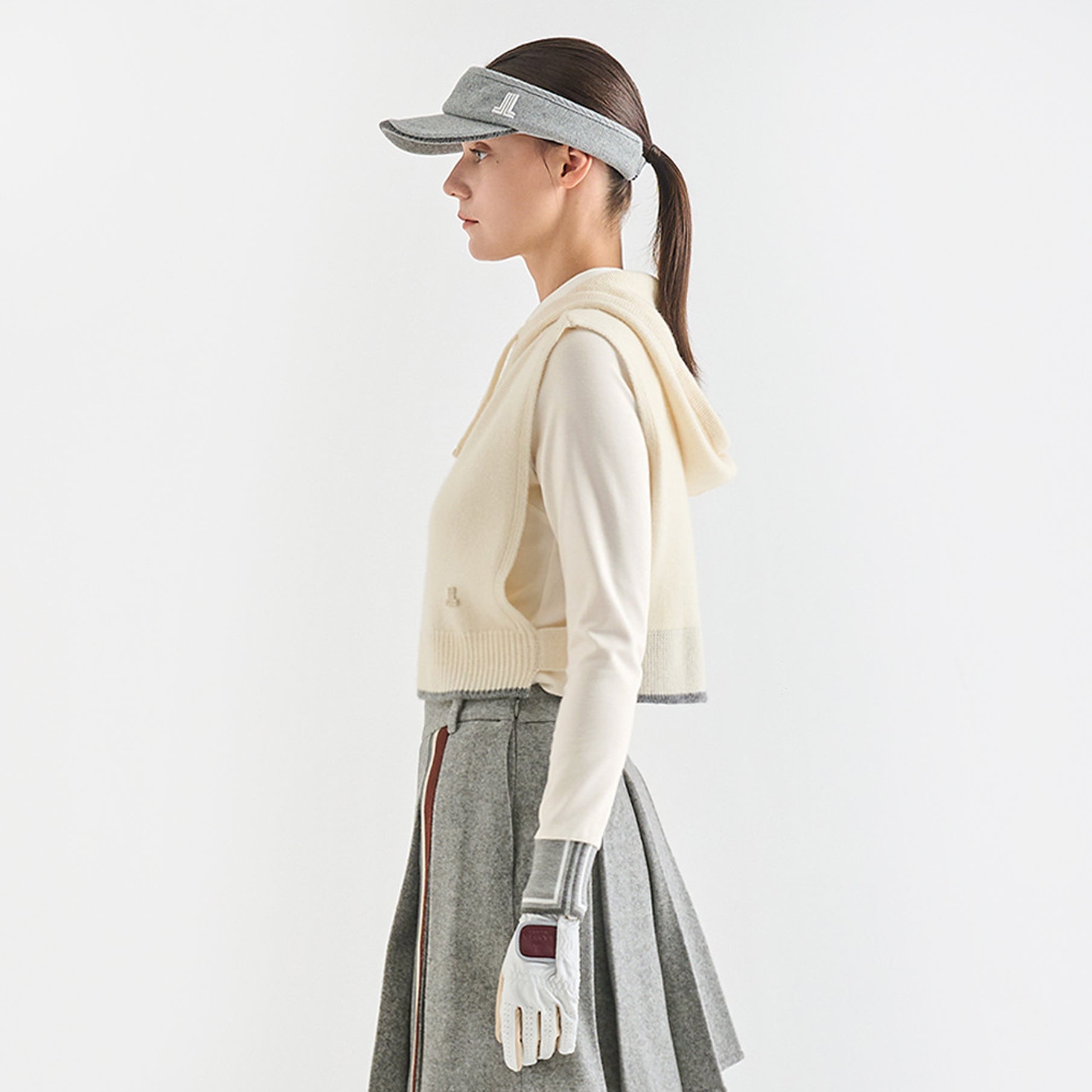 Woman wearing a visor, cardigan, skirt, and glove on a white background