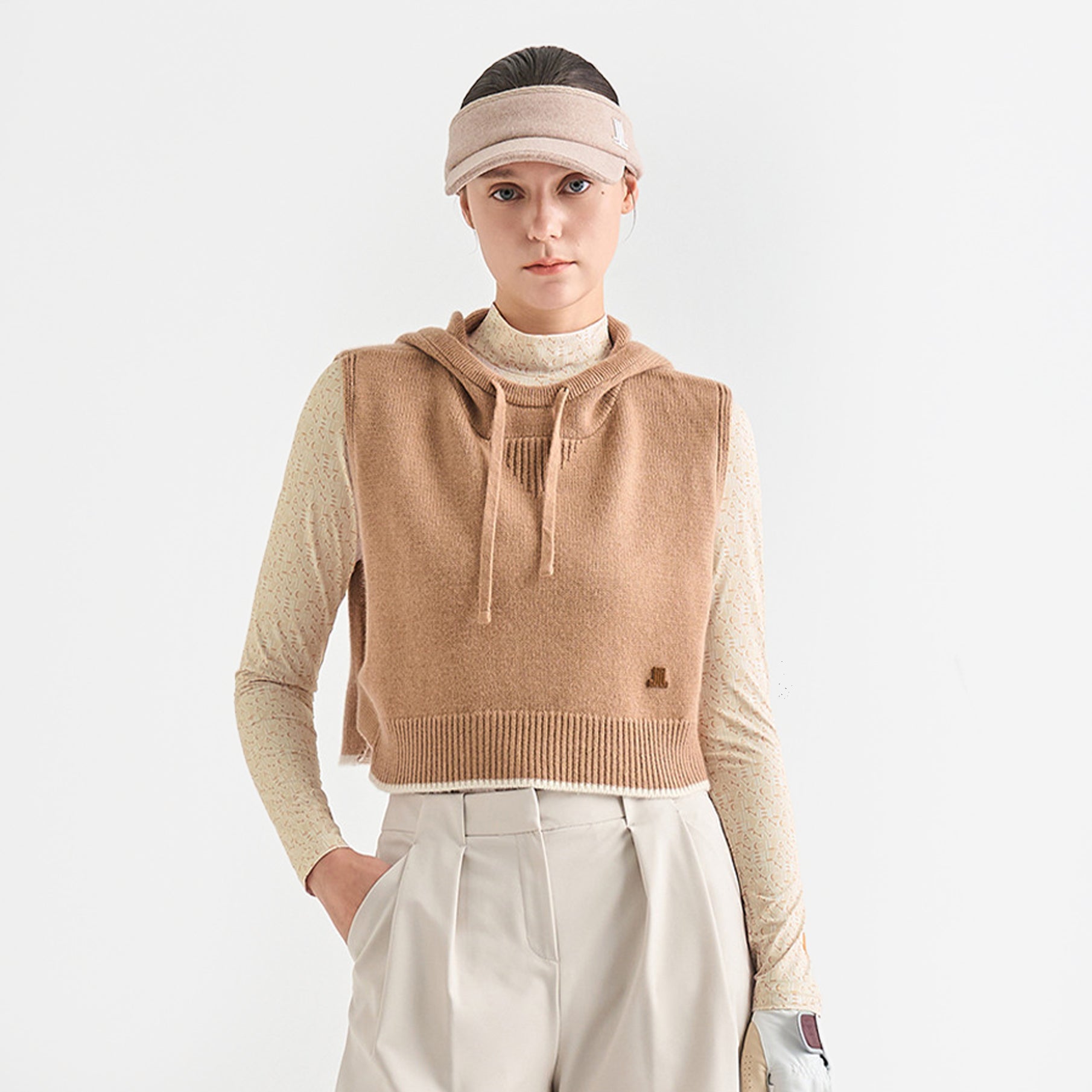 Person wearing a beige knitted vest over a long-sleeve shirt with a plain background
