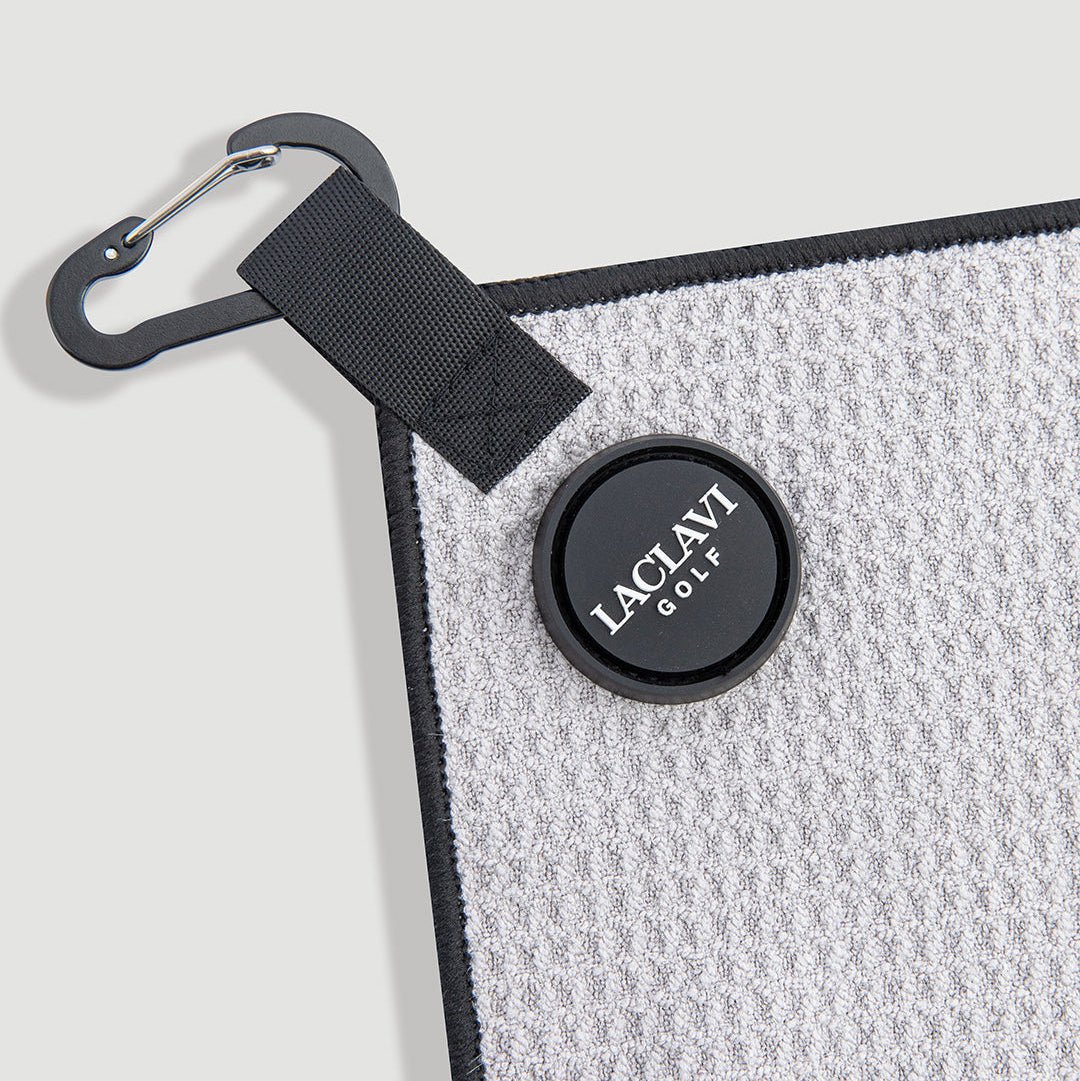 Close-up of gray golf towel corner with carabiner clip and round black Laclavi Golf magnetic marker - Laclavi Golf