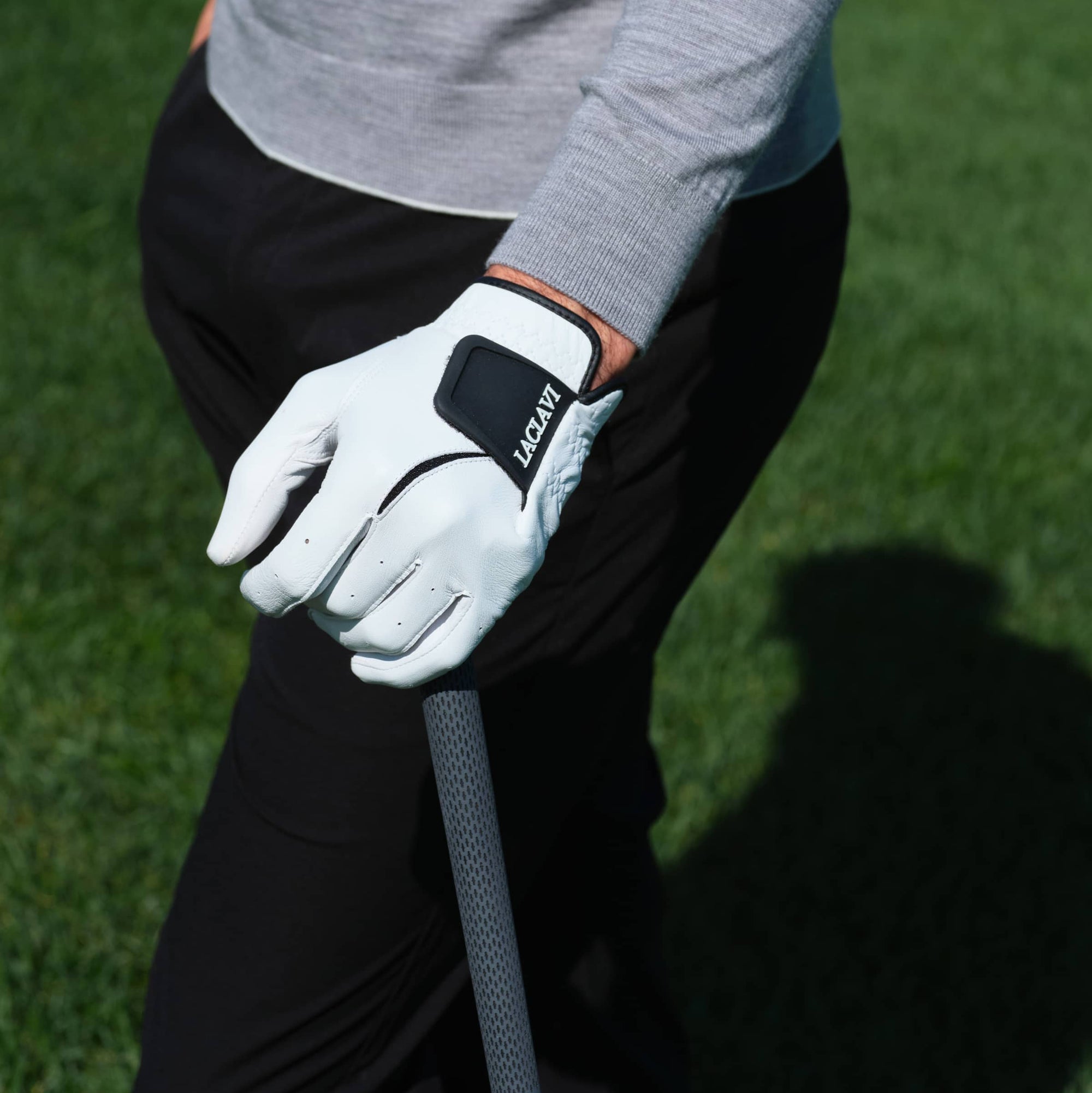 Golfer wearing white cabretta elite golf glove with black Laclavi strap gripping club on green course - Laclavi Golf