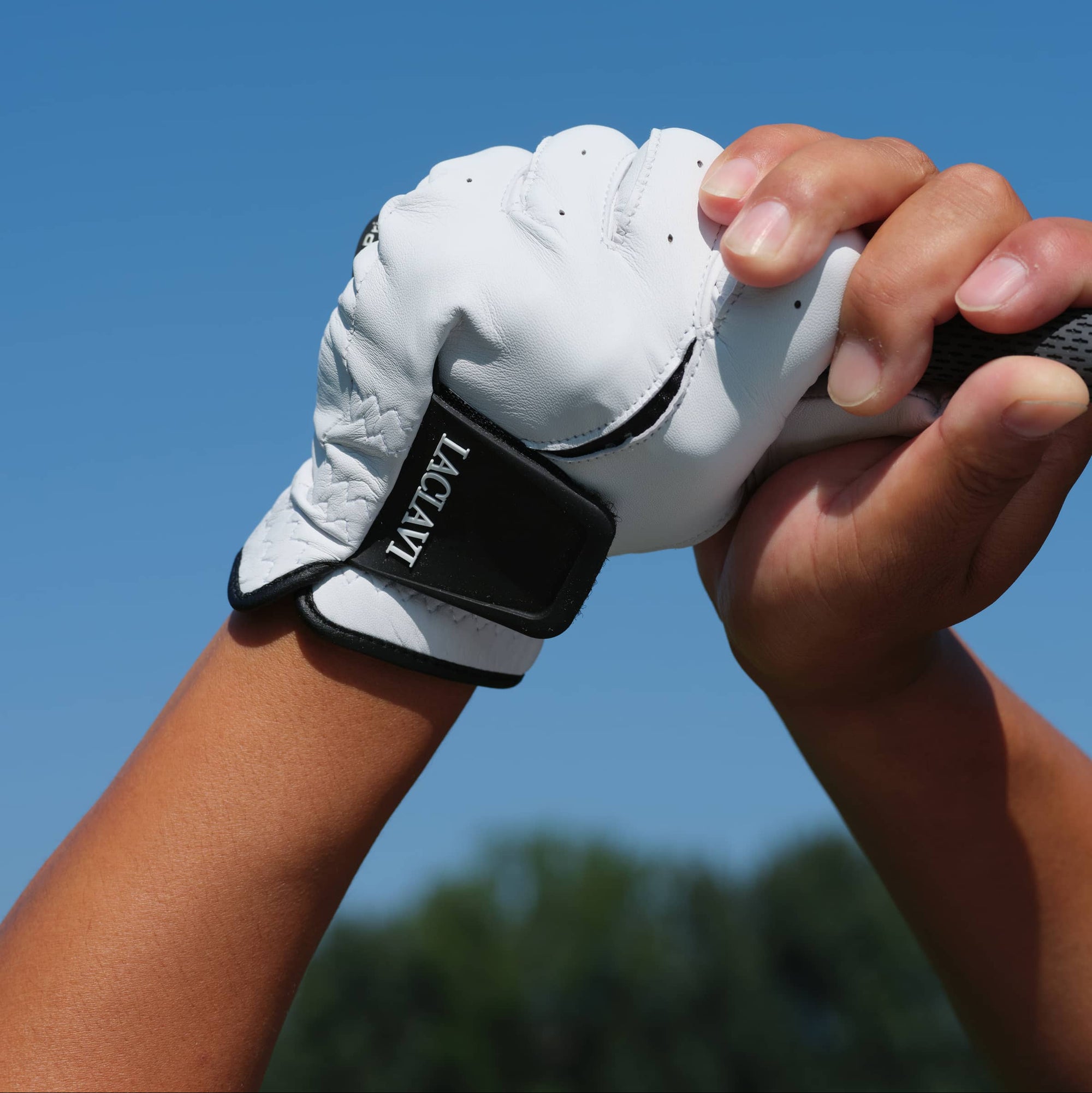 Golfer's gloved hand in white cabretta elite golf glove gripping club against blue sky outdoors - Laclavi Golf