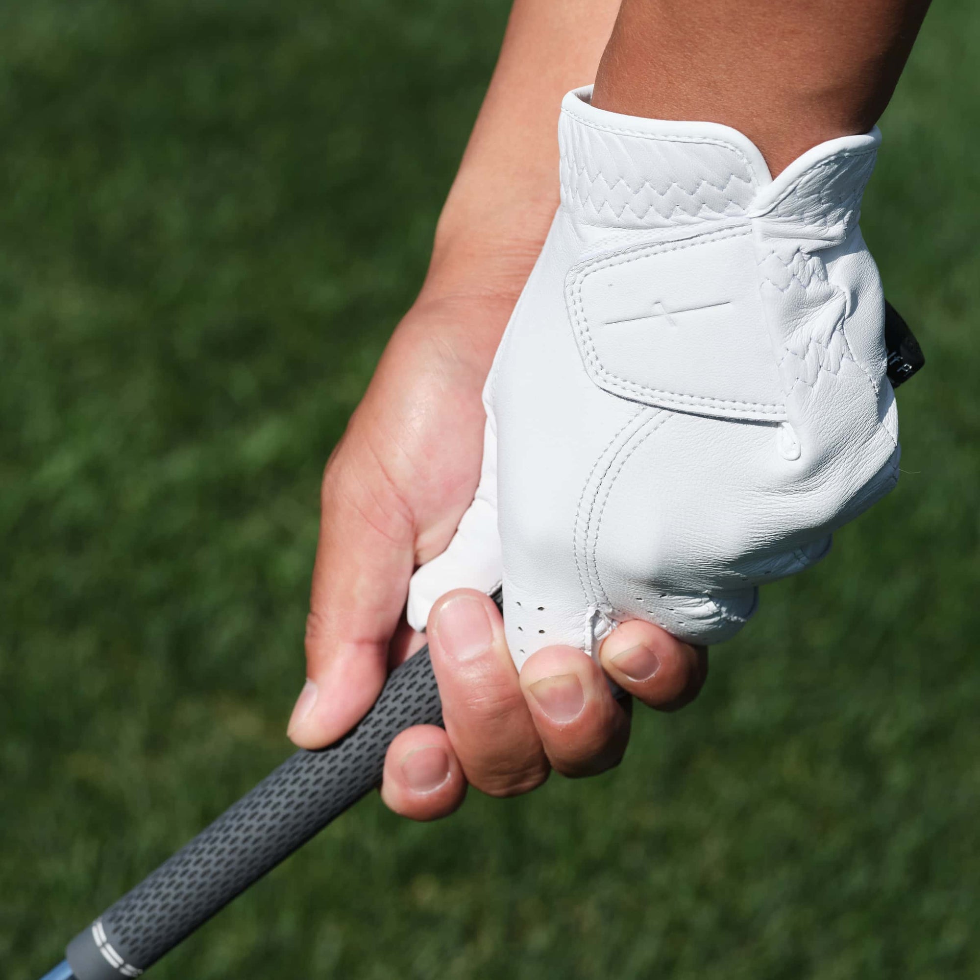 Golfer's hand wearing white cabretta tour golf glove gripping club on green fairway grass - Laclavi Golf