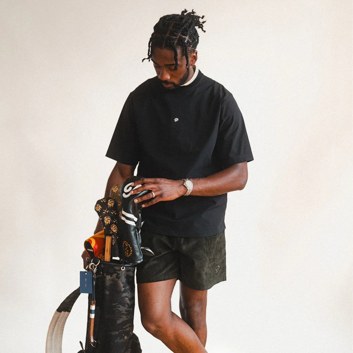 A man wearing a black golf shirt with golf clubs. 
