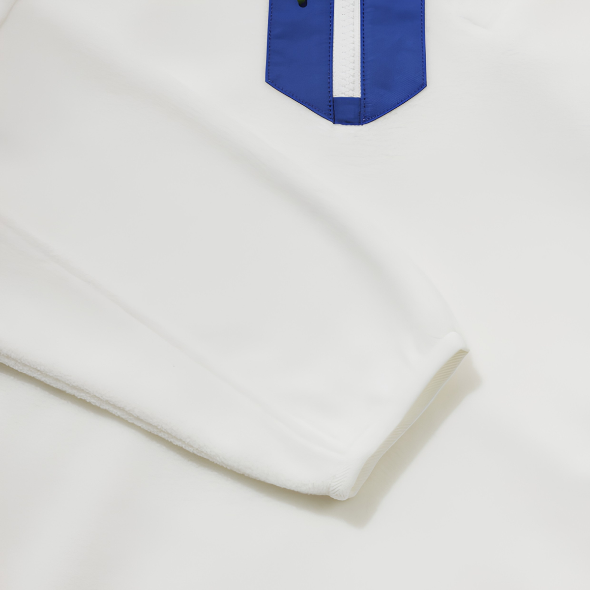 Close-up detail of a white long-sleeve garment, showing a folded cuff and a blue pocket with a white vertical stripe.